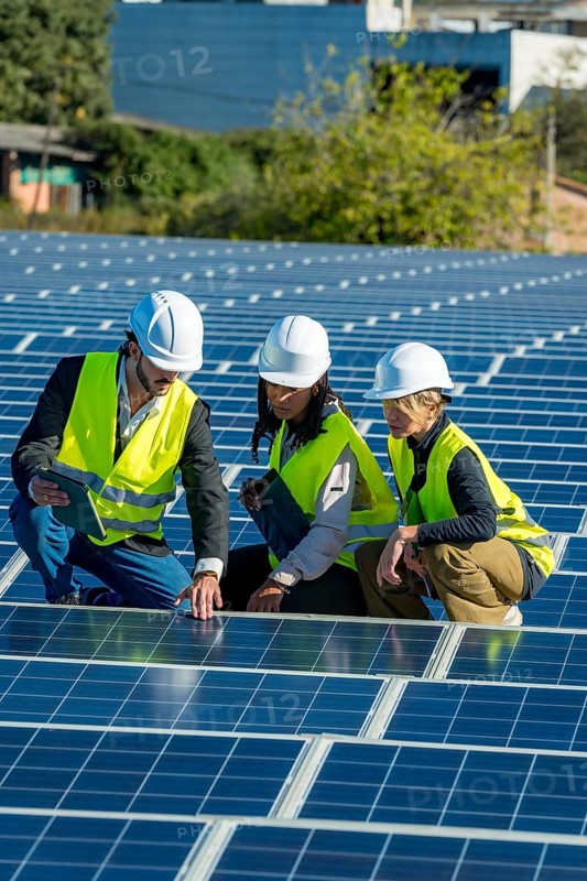 Diverse team of engineers and technicians inspecting and discussing solar panel installation and maintenance at a modern, sunlit solar farm focused on sustainable clean energy generation