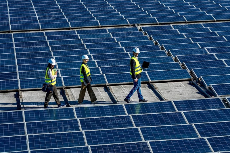 Three engineers walking on a rooftop solar power station, checking and inspecting the large array of photovoltaic panels, demonstrating teamwork in sustainable technology