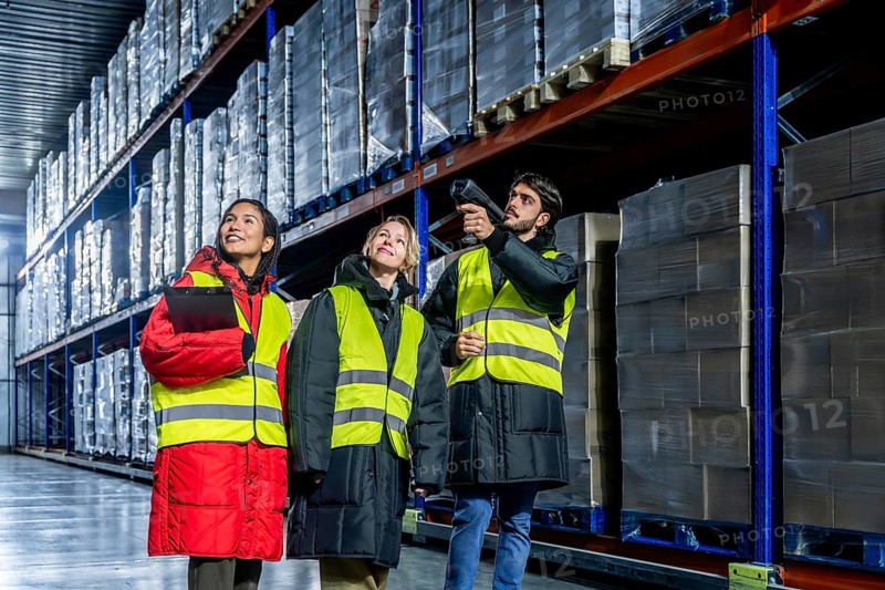 Diverse warehouse team in safety vests and warm protective gear scanning and checking inventory on high racks inside a large cold storage facility, ensuring efficient logistics and distribution