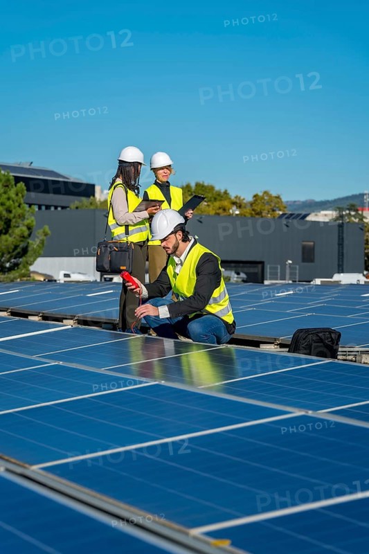 Engineers in hard hats and safety vests are examining solar panels on a rooftop, checking efficiency and ensuring proper function of the renewable energy system under a clear blue sky