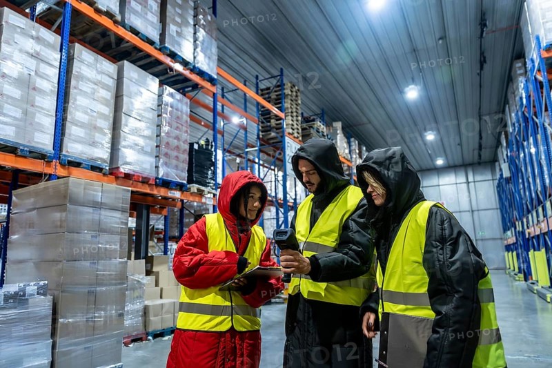 Diverse team in cold storage gear and high visibility vests using barcode scanner and tablet to coordinate inventory and shipments in a large frozen warehouse facility