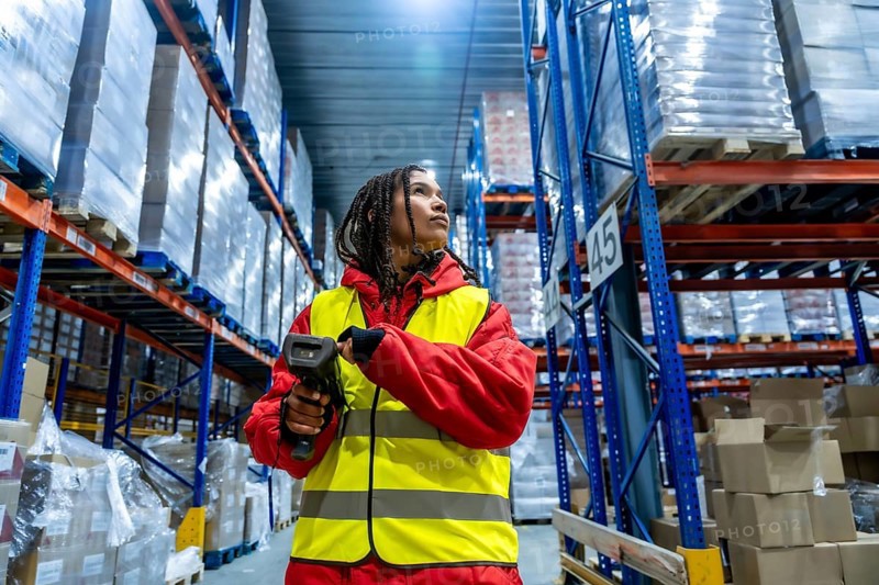 Worker in safety vest and warm jacket using a barcode scanner to manage inventory, ensuring efficient cold chain logistics and supply management in a large storage facility