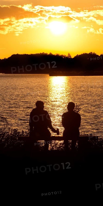 Two men sitting on a bench at sunset at Lake Gudelack, Lindow (Mark), Stechlin-Ruppiner Land nature park Park, Brandenburg, Germany