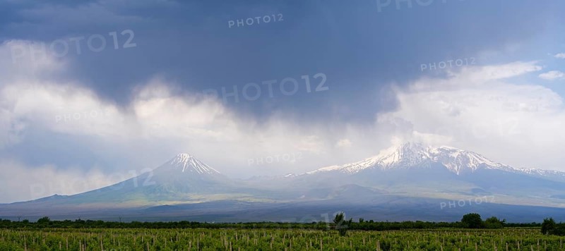 Two snow-capped mountains under dramatic skies with dark clouds over vast fields, Ararat and Little Ararat, located in Turkey, Ararat province, Armenia