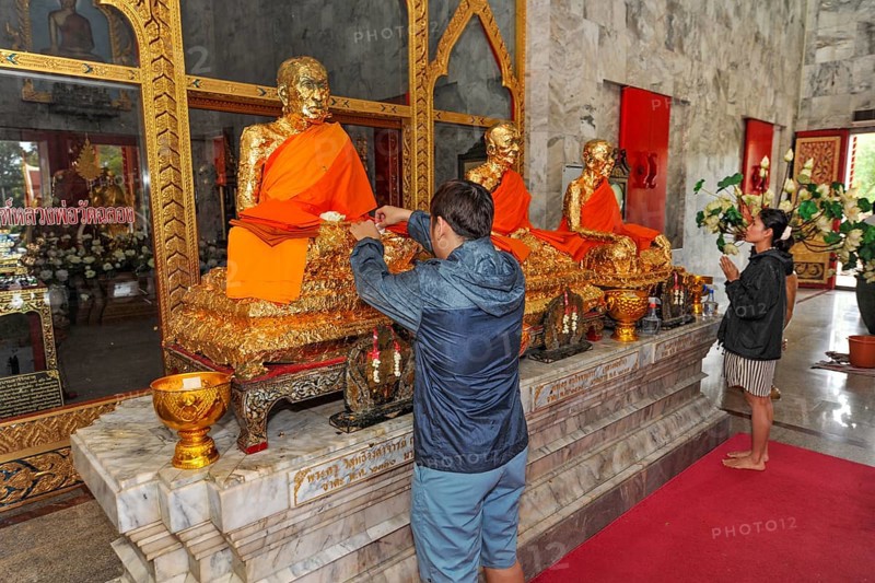 Buddhist believers Buddhists pray making offerings to statues of Buddhist monks covered with gold leaf at Wat Chalong Monastery, Phuket Island, Phuket Province, Thailand