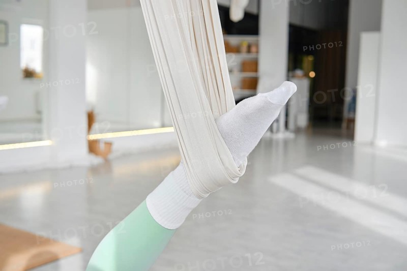A person engages in fitness stretching using a hammock for support. The scene is set in a bright studio with natural light, enhancing the atmosphere of wellness and relaxation during workout