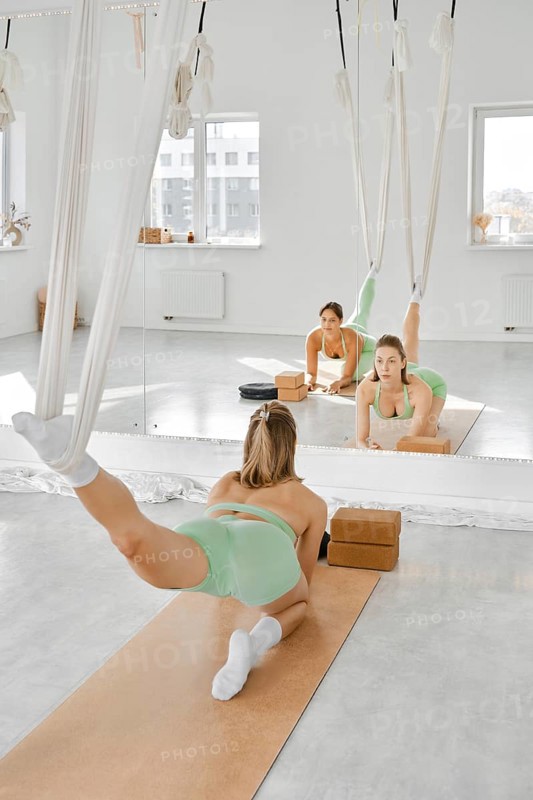 A woman is engaged in a leg stretching fitness routine using a hammock in a well-lit studio