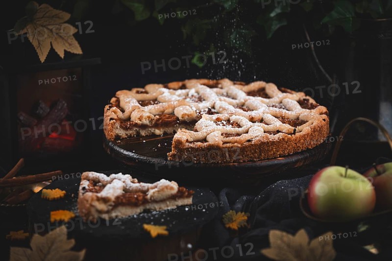Icing sugar falls on apple pie surrounded by autumn leaves in a dark environment