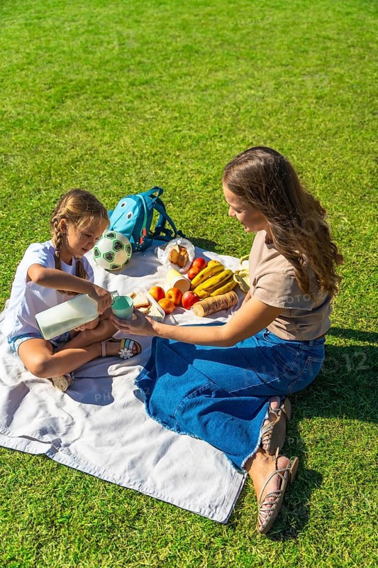 Mother and daughter enjoying a summer picnic in a lush green park, sharing healthy food, fruit, and milk in a natural environment, fostering family connection and wellness