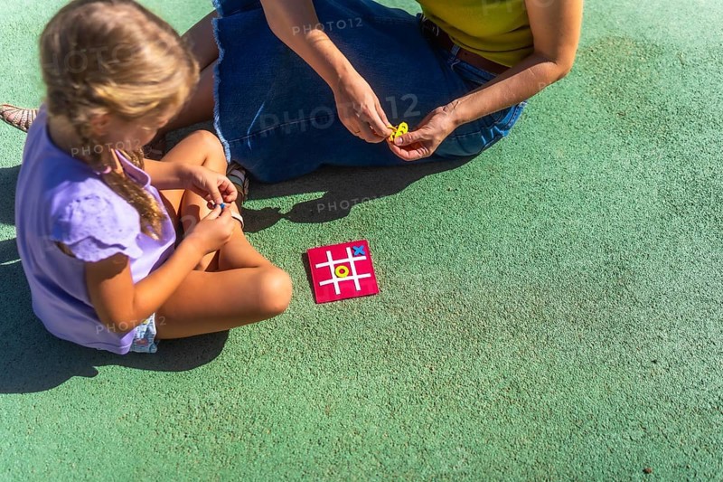 Mother and daughter bonding over a game of tic tac toe on a sunny day, enjoying quality family time and childhood leisure activities in a park setting