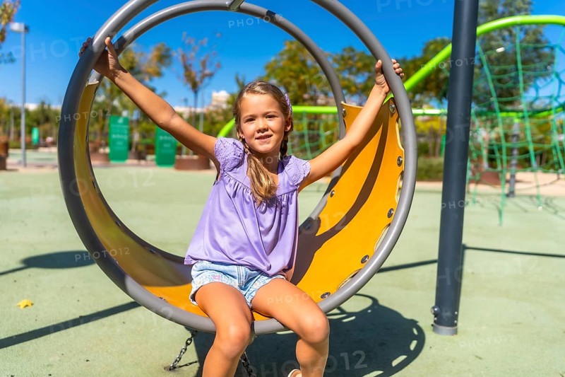 Happy child swinging on a round playground swing, enjoying outdoor activity on a sunny day, experiencing joy and carefree childhood moments at the park