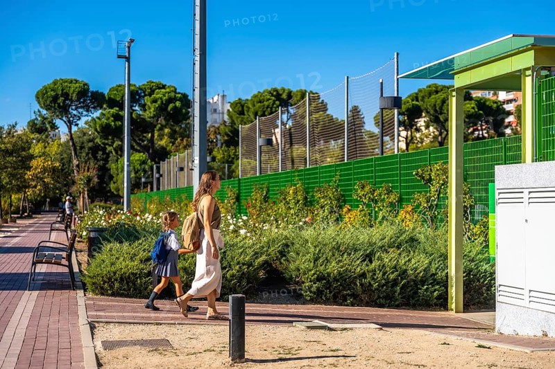 Mother and daughter walking together on a sunny day, the young student wearing a backpack and uniform, heading towards school, symbolizing education, family support, and a new school year