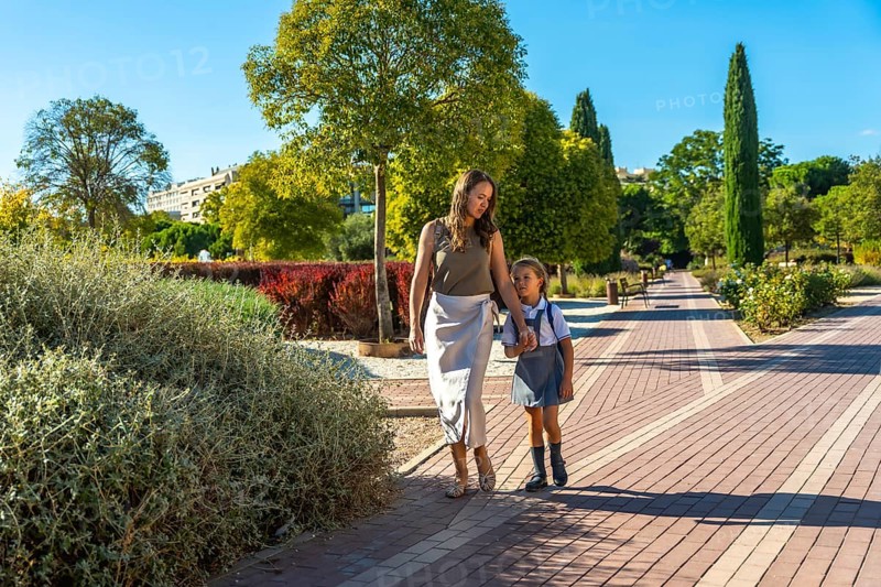 Mother and daughter walking along a path in a park, holding hands and going to school on a sunny day, representing family, education, and early childhood