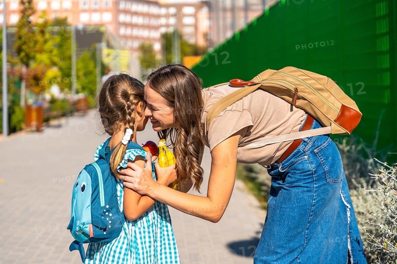 Loving mother bending down to embrace her small daughter with a backpack on the first day of school, showing care and emotional connection as the child prepares for new learning