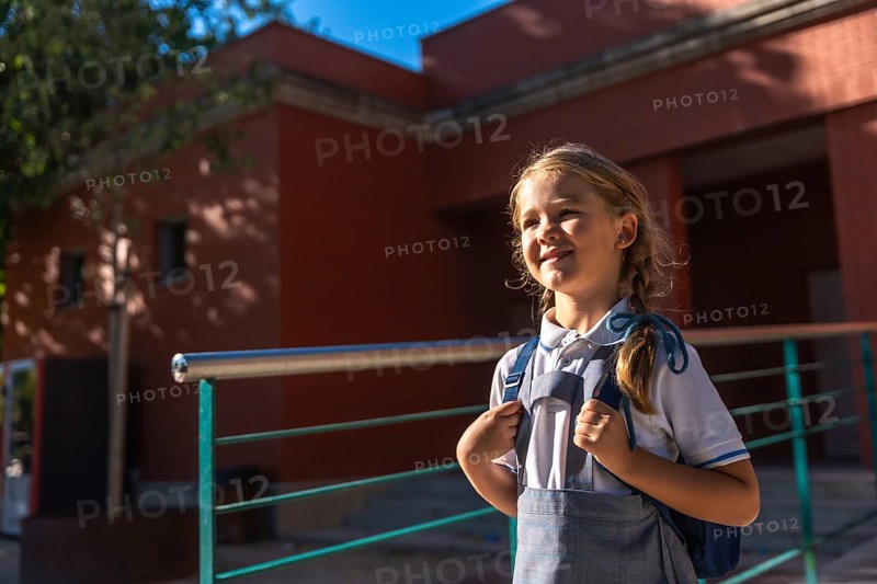 Young happy girl student wearing a school uniform and backpack, ready for the first day of school or returning from summer holidays, standing outdoors looking to the future