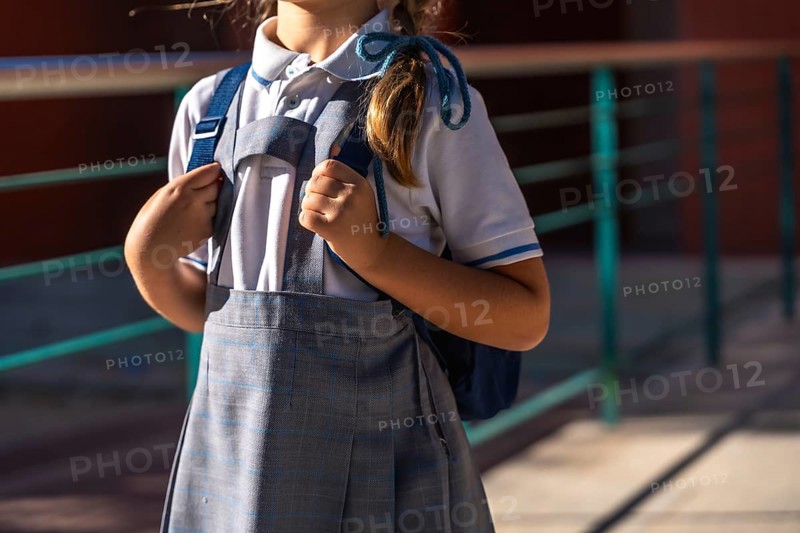Young student in school uniform stands outdoors on a sunny day holding a backpack, ready and prepared for the first day of classes and a new academic year