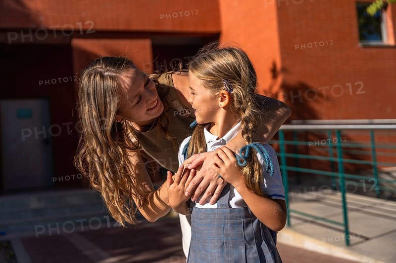 Woman tenderly hugging her daughter wearing a school uniform, sharing a loving moment outside the school building, symbolizing back to school and family support