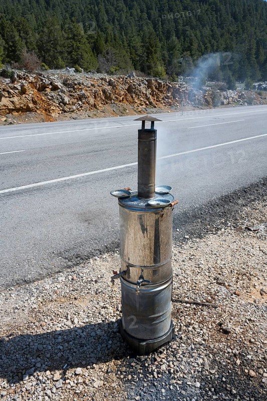 Smoking metal stove with roadside chimney against wooded backdrop, traditional samovar, kettle for making tea, powered by wood, on the side of the road on the D695 near Akseki, Antalya province, Turkey
