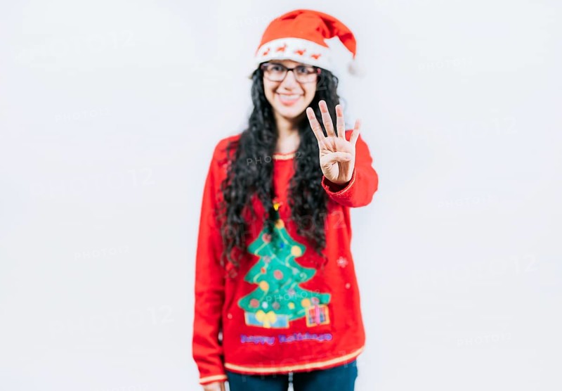 Smiling girl in Christmas sweater counting number 4. Happy girl in Christmas hat counting number FOUR, isolated