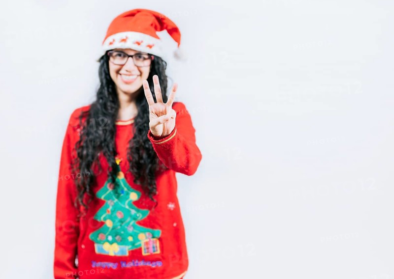 Smiling girl in Christmas sweater counting number 3. Happy girl in Christmas hat counting number THREE, isolated