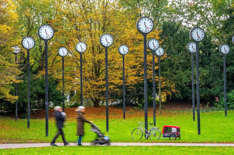 The art installation Zeitfeld in Volksgarten Park in Düsseldorf-Oberbilk, a total of 24 station clocks, on 6 meter high steel columns, have been running synchronously since 1987, walkers in the municipal park, artwork by Düsseldorf artist Klaus Rinke, symbol of time, time change, North Rhine-Westphalia, Germany