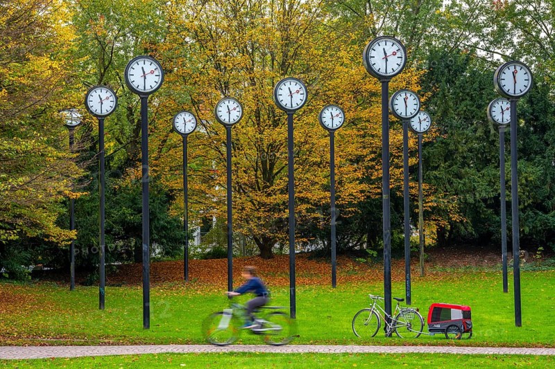 The art installation Zeitfeld in Volksgarten Park in Düsseldorf-Oberbilk, a total of 24 station clocks, on 6 meter high steel columns, have been running synchronously since 1987, cyclists in the municipal park, artwork by Düsseldorf artist Klaus Rinke, symbol of time, time change, North Rhine-Westphalia, Germany