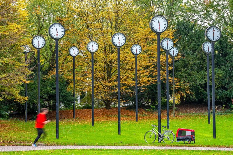 The art installation Zeitfeld in Volksgarten Park in Düsseldorf-Oberbilk, a total of 24 station clocks, on 6 meter high steel columns, have been running synchronously since 1987, jogger in the municipal park, artwork by Düsseldorf artist Klaus Rinke, symbol of time, time change, North Rhine-Westphalia, Germany