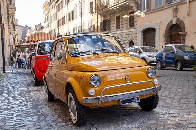 A yellow Fiat 500 is parked in an alley in central Rome
