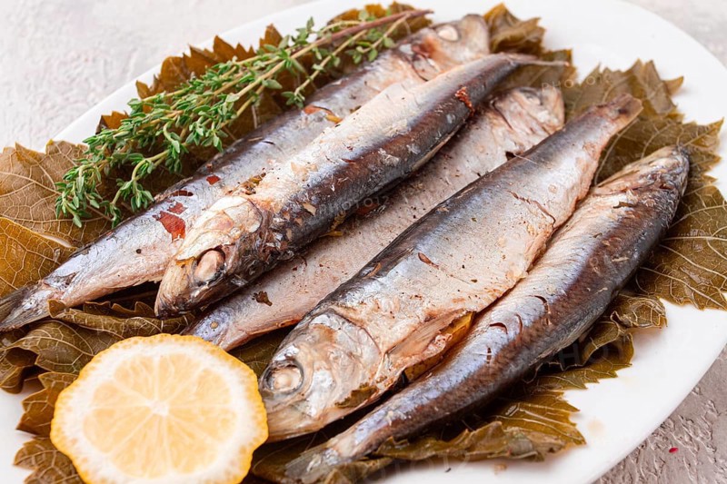 Baked fish, in grape leaves, with spices, on a white plate, homemade