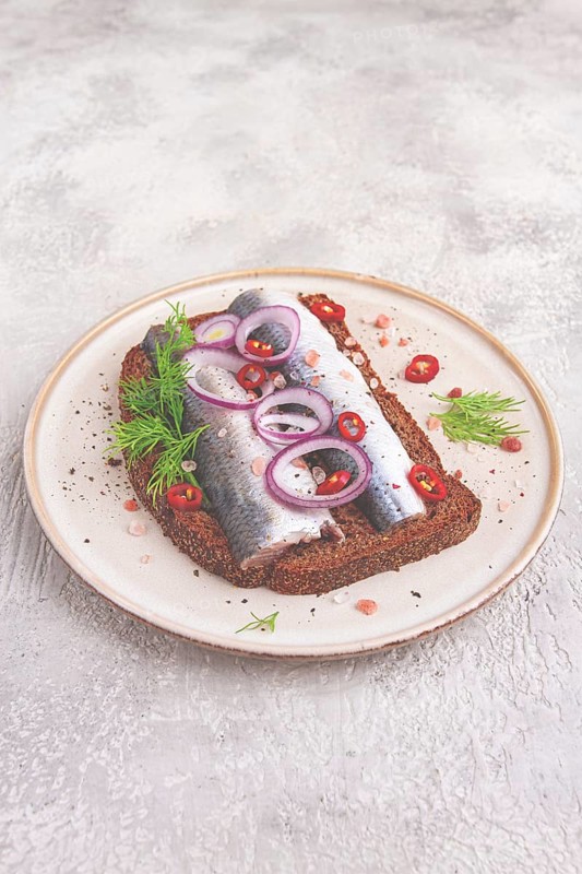 Sandwiches, Herring fish, on dark rye bread, sprinkled with onion, chili pepper and herbs, on a light plate