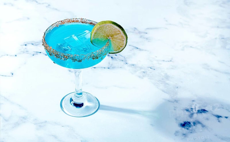 Bright blue cocktail with a slice of lime on a marble surface