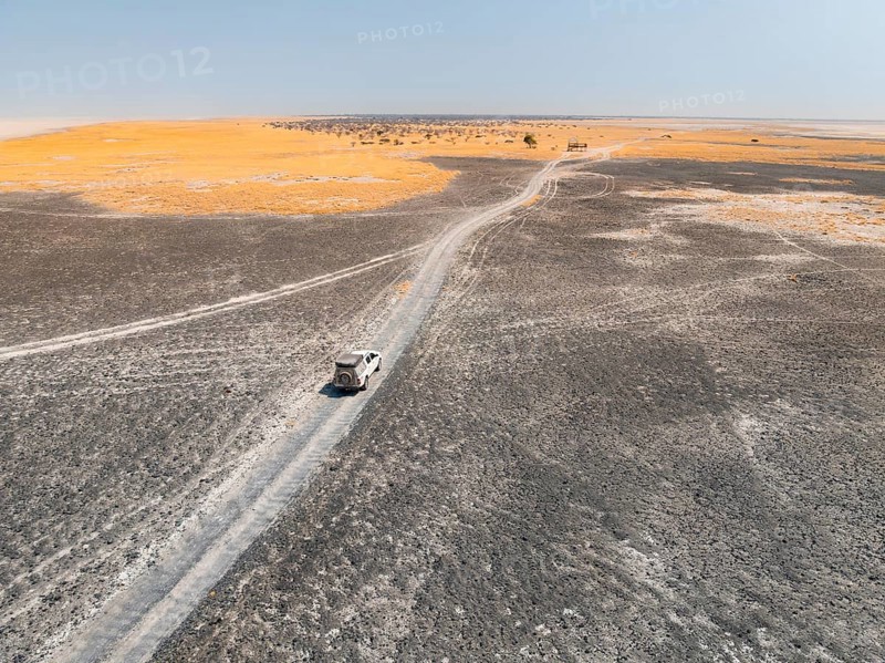 Aerial view of off-road car driving on a salt pan, arid landscape, Botswana