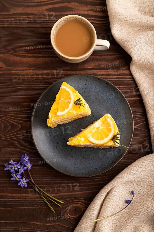 Lemon cake on brown wooden background and linen textile, cup of coffee, top view, flat lay, close up