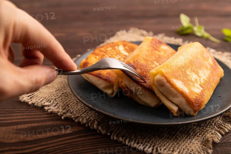 Fried crispy pancakes with meat and cheese with hand on brown wooden background and linen textile. side view, close up, selective focus