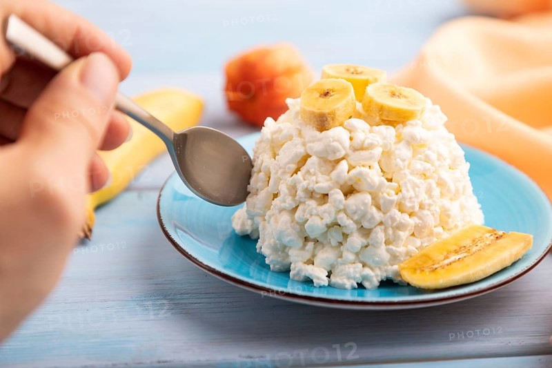 White ?ottage cheese, Curd, with Banana with hand on blue wooden background and orange textile, side view, close up, selective focus