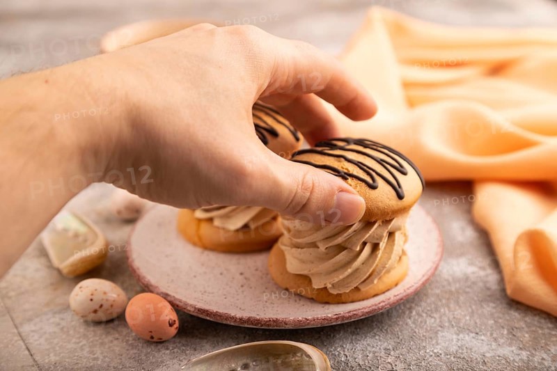 Caramel Cream Cakes with hand on brown concrete background, cup of coffee, side view, close up, selective focus