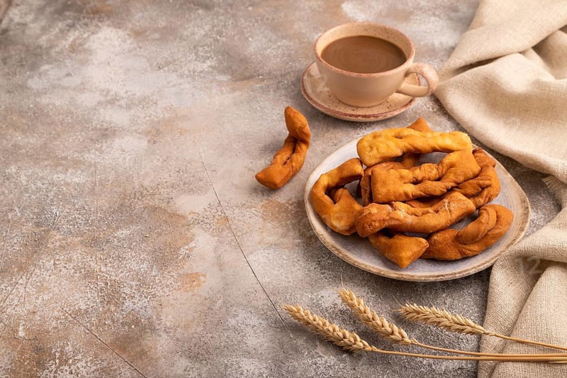Crunchy biscuit Brushwood cookies sprinkled with powdered sugar on brown concrete background and linen textile, cup of coffee, side view, copy space