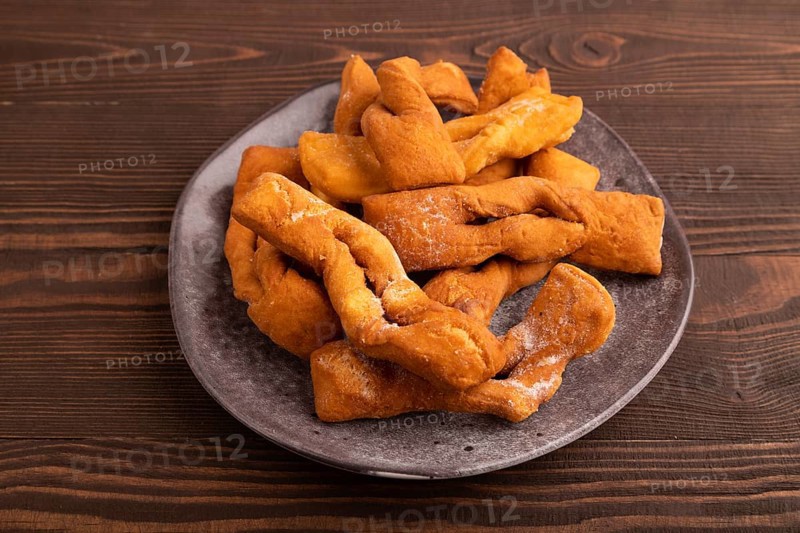 Crunchy biscuit Brushwood cookies sprinkled with powdered sugar on brown wooden background, side view, close up