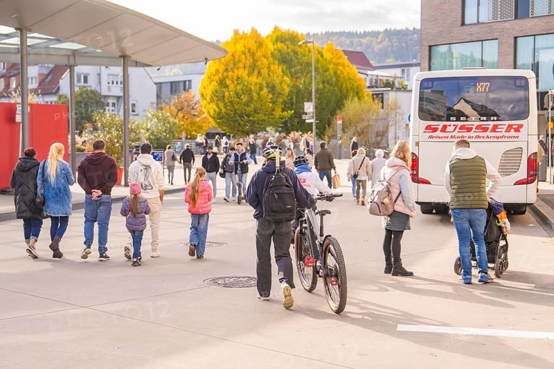 Busy scene at a bus stop, people on the move, a cyclist pushes his bike, Urschelherbst street festival, Nagold, Germany