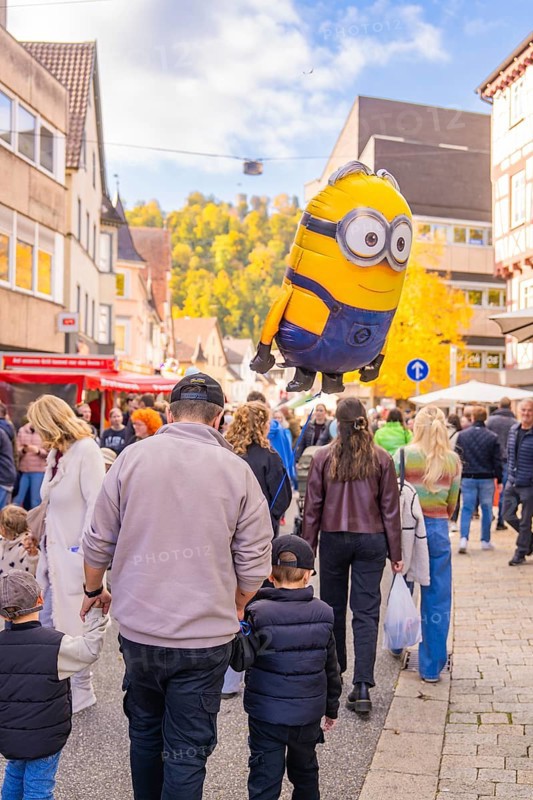 A minion balloon hovers over a family strolling through the city in sunny autumn, Urschelherbst street festival, Nagold, Germany