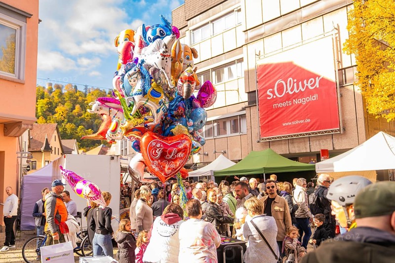 Colourful balloons over a crowd of people on a sunny market square surrounded by buildings, Urschelherbst street festival, Nagold, Germany