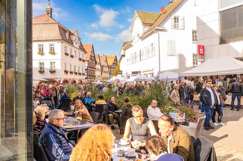 People sit in a street café in an old town under sunny skies. Busyness and convivial atmosphere prevail, Urschelherbst street festival, Nagold, Germany
