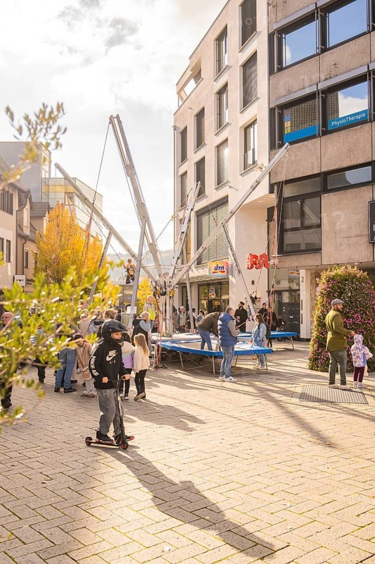 A group of people gather around bungee trampolines in an urban area, Urschelherbst Street Festival, Nagold, Germany