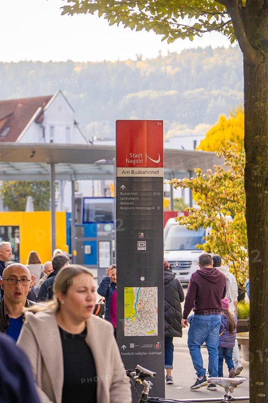 People walk past a bus stop, a signpost shows the way, Urschelherbst Street Festival, Nagold, Germany