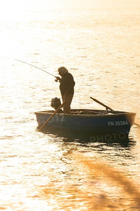 Single fisherman in a small boat fishing in the setting sun, Überlingen, Lake Constance, Germany