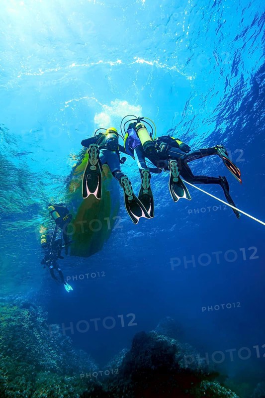 Underwater photo Group of scuba divers climb up to the sea surface at the end of dive on anchor rope from small boat dive ship, Mediterranean Sea, Majorca, Spain