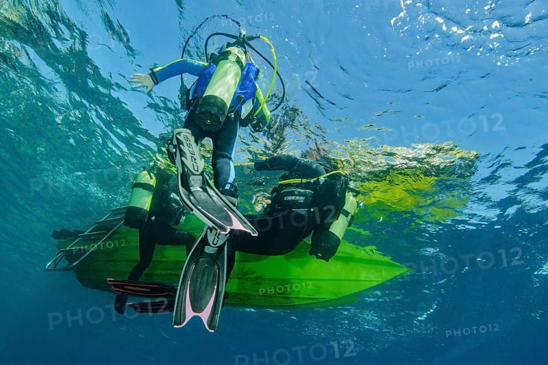 Underwater photo Group of scuba divers climb up to the sea surface at the end of dive on anchor rope from small boat dive ship, Mediterranean Sea, Majorca, Spain