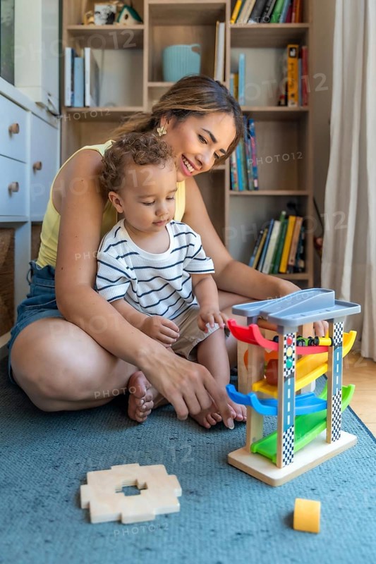Smiling mother and son playing with a toy car and garage, enjoying quality time together in their living room