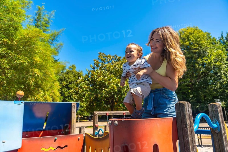 Happy mother holding her smiling son on a colorful playground game structure on a sunny summer day