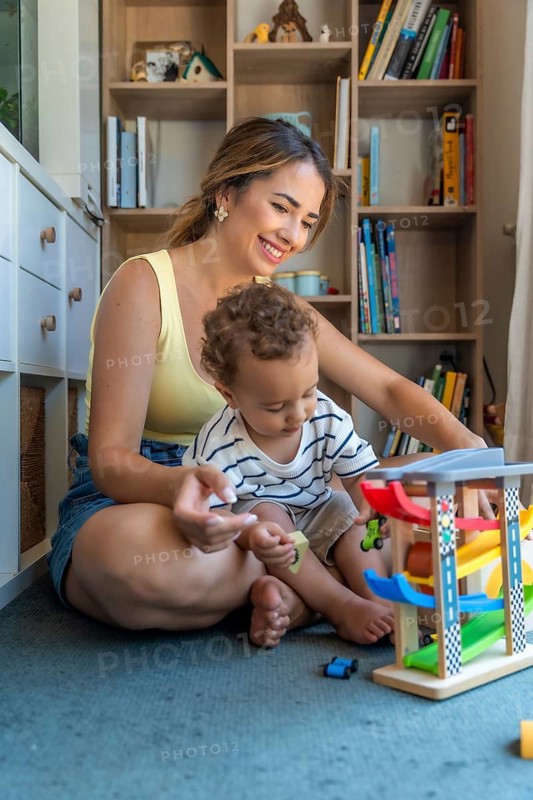 Happy mother and son playing with toy cars and garage, sitting on the floor in the playroom, having fun together